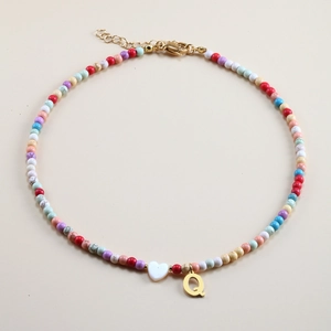 Detail of colorful beaded necklace with golden letter Q pendant and white heart bead