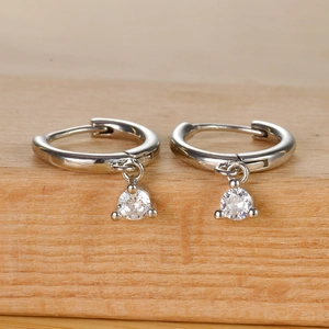 Detail of silver hoop earrings with clear round cubic zirconia charms on wood base