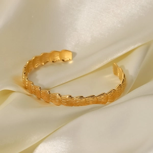 Détail du bracelet ouvert doré à texture ondulée sur un tissu en satin beige