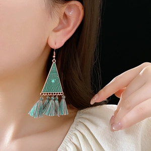 Detail of bohemian triangle drop earrings with green tassels worn by a model