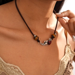 Macro detail of tiger eye beads and strawberry charm on a retro brown woven necklace