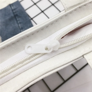Detailaufnahme eines weißen Kunststoffreißverschlusses an einer beigen Segeltuchtasche