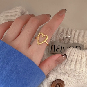 Detail of minimalist gold and silver open heart rings worn with a stylish knit sweater
