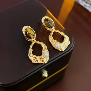 Gold-plated oval tiger eye earrings with pearl detail and pleated metal on a jewelry box