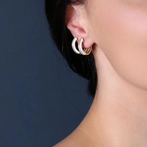 Eleganti orecchini a cerchio dorati con smalto bianco e zirconi indossati da modella