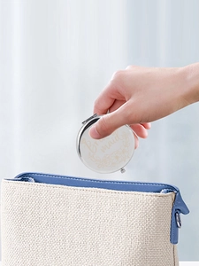 Putting round metal bridesmaid compact mirror with flower engraving into a small handbag