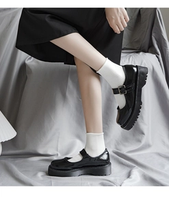 Dettaglio scarpe Mary Jane nere con plateau, fibbia metallica e calze bianche con volant