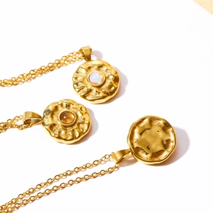 Detail of gold coin pendants with hammered texture and colorful birthstones on white surface