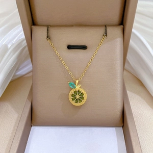 Detailed view of a gold fruit slice necklace with green stones in a gift box
