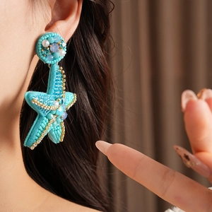 Macro detail of a large turquoise starfish earring featuring handmade beadwork and crystals