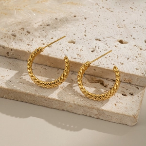 Close-up of golden triple-layered twisted hoop earrings on textured stone surface