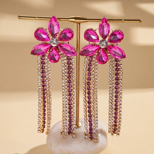 Détail de boucles d'oreilles à fleurs fuchsia et pompons avec strass sur socle doré