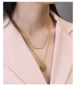 Double-layered gold necklace set with bar and round relief charms on female model