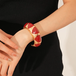 Detail of red enamel triangle cuff bracelet with gold brushed metal texture on wrist