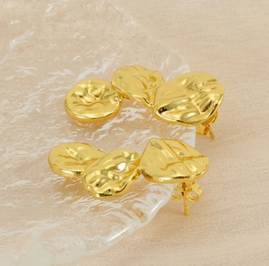 Macro view of gold irregular petal earrings with textured surface on a glass tray