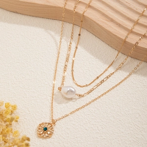 Detail of gold layered necklace with baroque pearl and green rhinestone flower pendant