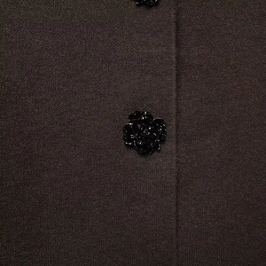 Close-up of decorative black floral button on a dark brown knit blazer fabric