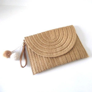 Detail of paper straw woven clutch featuring dual-tone pompom and wrist strap