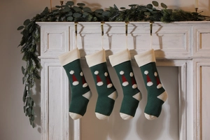 Detail of four green knitted Christmas stockings with red hat patterns hanging on a fireplace