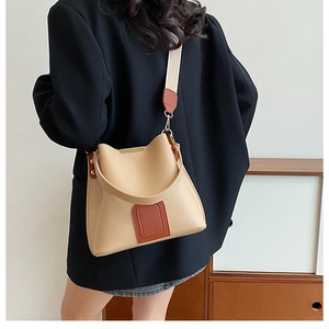 Detail view of khaki bucket bag with wide shoulder strap worn over a black blazer