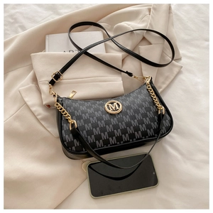 Detail of retro black underarm bag with M-pattern print and gold metallic logo