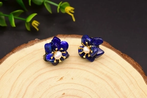 Detail view of blue stone flower earrings with white pearl center on wooden display