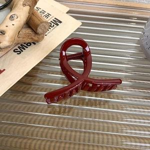 Close-up of a festive deep red hair claw clip on a stylish glass surface with props
