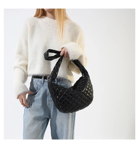 Detail of a black quilted half-moon shoulder bag styled with a white knit sweater