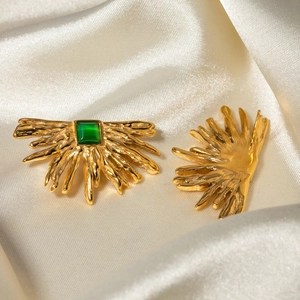 Macro shot of gold sunburst earring featuring a square green gemstone on white silk