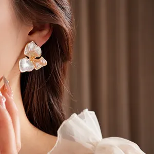 Elegant pearl white flower earrings with gold edges worn by a model in a close-up shot