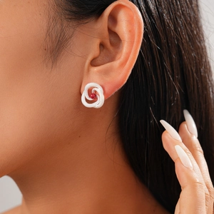 Close-up of a silver twisted knot earring featuring a central round red gemstone inlay