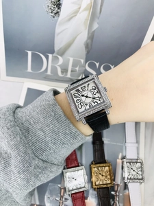Detalle de reloj cuadrado con cristales, números artísticos y correa de cuero en la muñeca