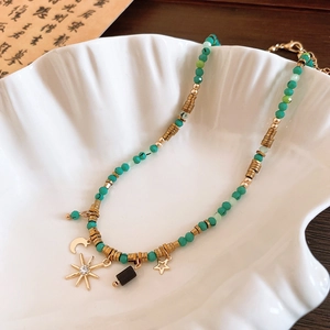 Detailed shot of green beaded necklace with gold moon and sun charms in a shell tray