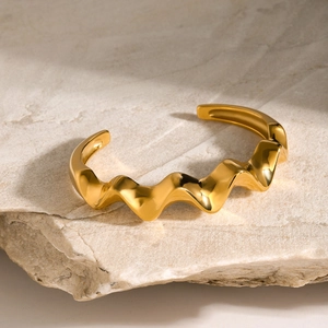 Detail of 18k gold plated stainless steel wavy open bangle on natural stone background