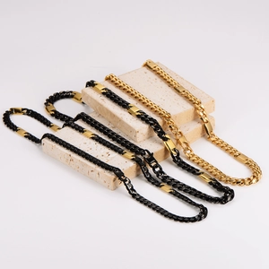 Two-tone gold and black stainless steel Cuban link necklaces on stone display