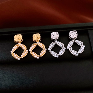 Detail of square gold and silver earrings with small white pearls on a display tray