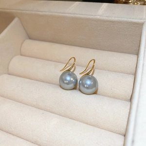Close-up of 18K gold S-shaped hooks with lustrous grey pearls on beige velvet