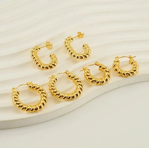 Detailed view of three pairs of twisted gold hoop earrings on a white textured tray