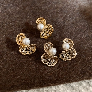 Detail showing gold hollow earrings with pearls on dark brown plush background