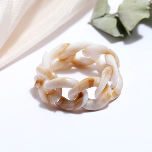 Close-up of chunky resin chain ring with amber marble texture on cream silk fabric