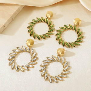 Elegant gold flower wreath earrings with green and clear leaf crystals on silk background