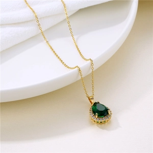 Gold necklace with emerald teardrop pendant and small diamonds on a white plate