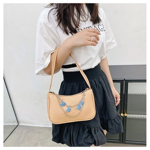Beige underarm bag with blue butterfly metal chain detail shown on a model