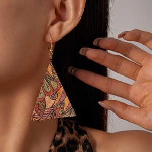 Détail de boucles d'oreilles triangulaires en cuir aux motifs abstraits et crochets dorés