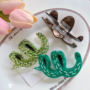 Trois pinces à cheveux en acétate en forme de serpent sur une assiette blanche décorative