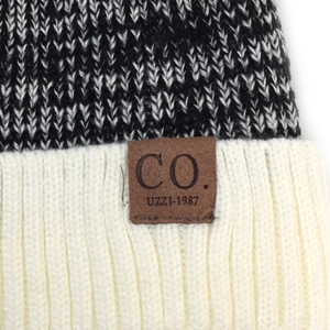 Macro detail of men's winter knit beanie showing black and white texture and leather logo