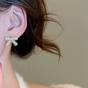 Close-up of model wearing gold-plated bow earrings with white cubic zirconia stones