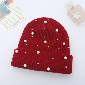 Detail of red cable-knit beanie with white pearls and metal beads on a white background