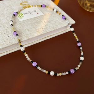 Detail of beaded necklace with pearls, purple and black beads on linen texture