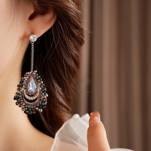Close-up of teardrop tassel earrings with colorful crystals worn on a model